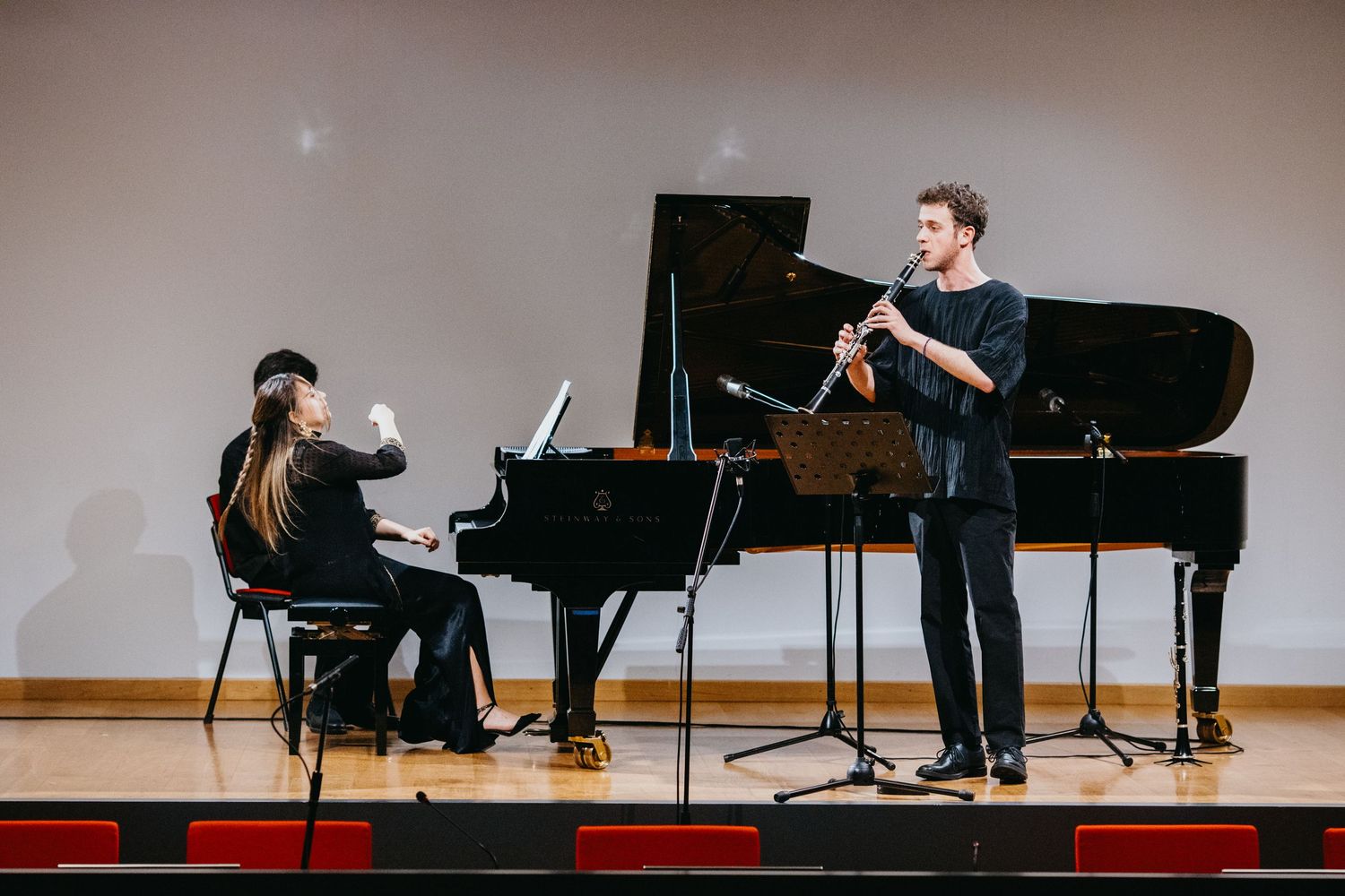 Male clarinetist performs with female pianist accompanist on grand piano during recital.