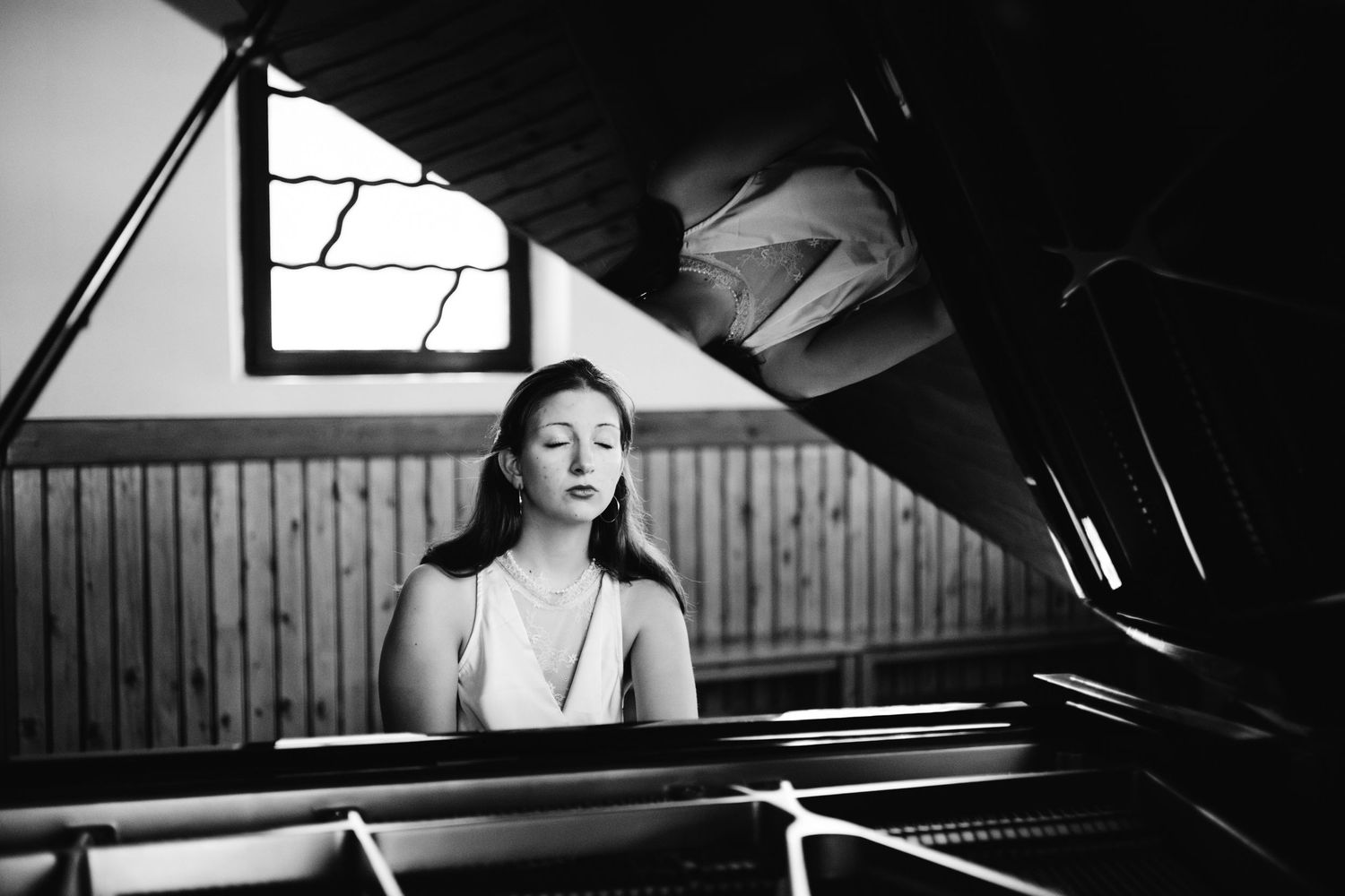 Young woman playing a grand piano in a black and white photo inside a wooden room.
