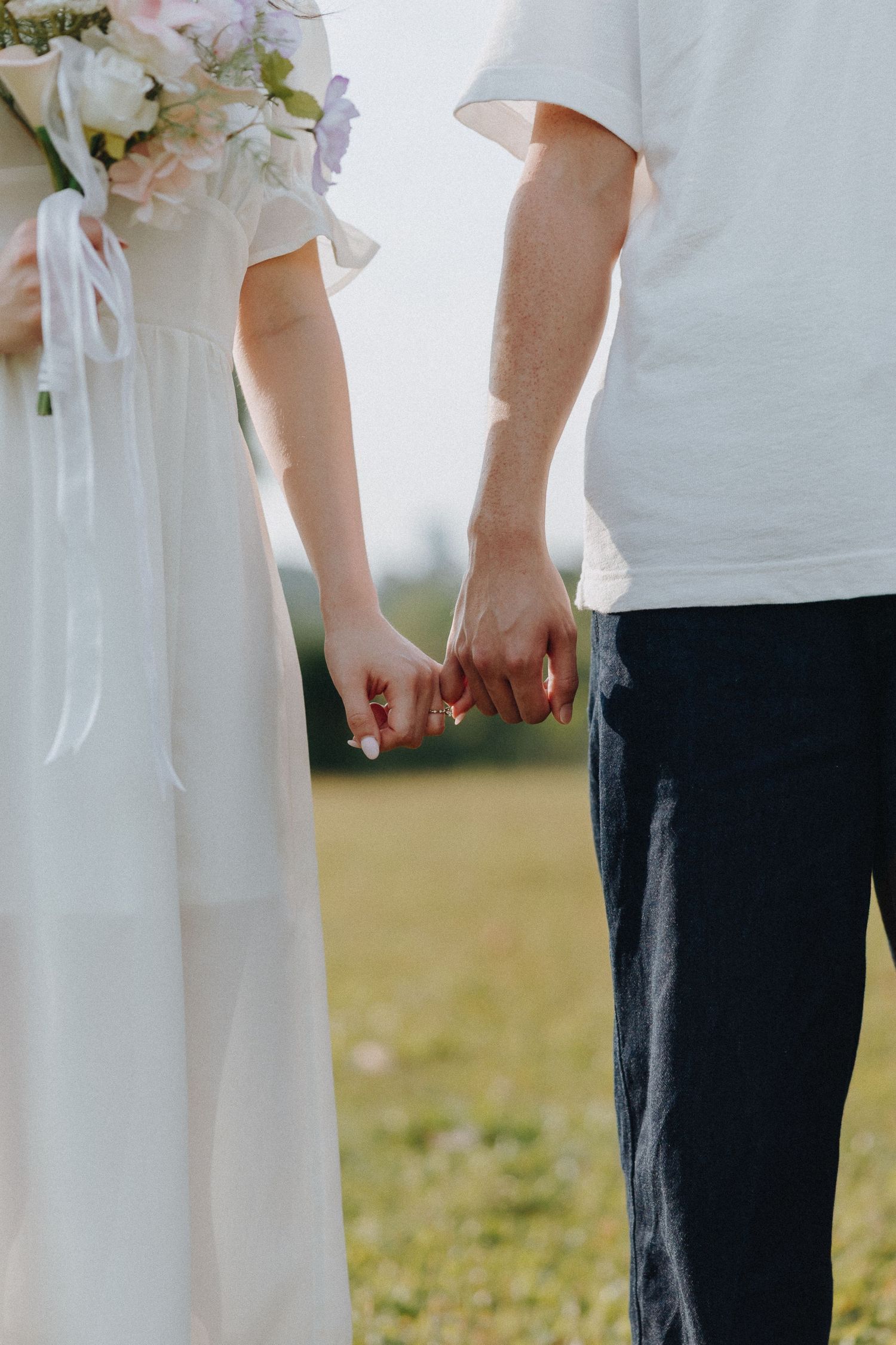 Close-up shot of a couple holding hands in white and navy outfits against a grassy background.