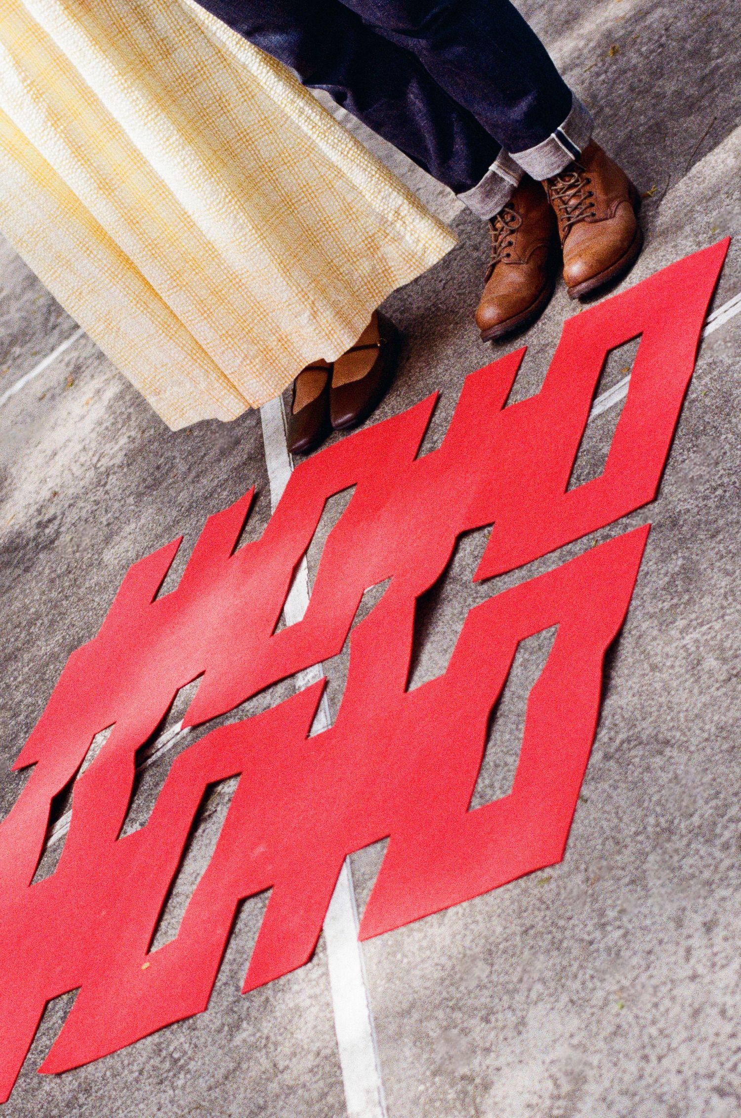 Close-up of brown leather boots walking across red letters on a concrete floor.