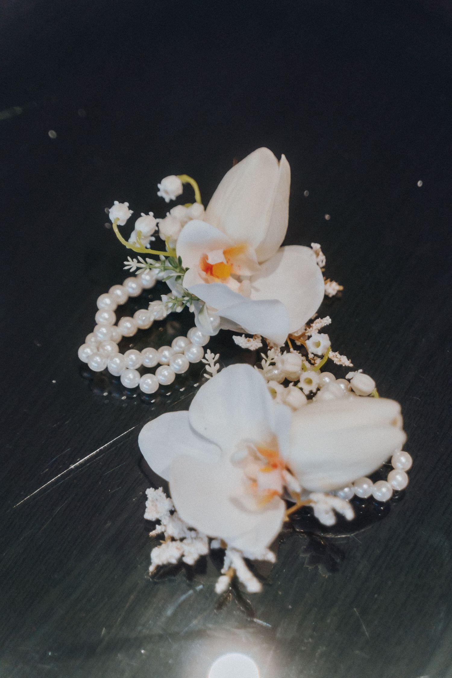 Delicate white orchid flowers arranged with pearl strands and baby's breath on a dark surface.