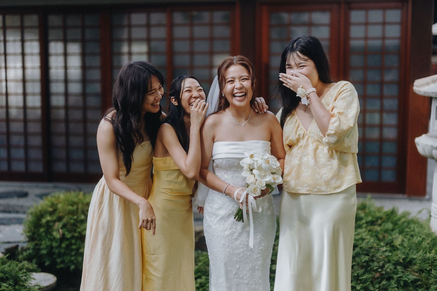 Wedding party in yellow and white dresses poses together in an outdoor garden setting.