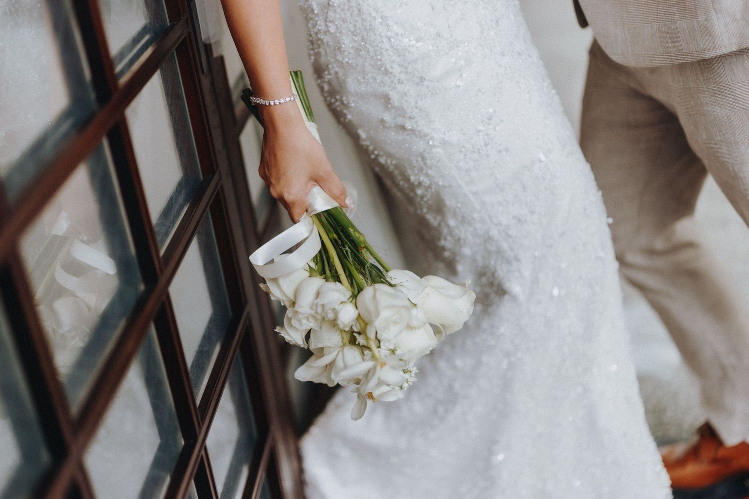 Elegant white tulip bouquet held against a textured wall in a bridal wedding photo.