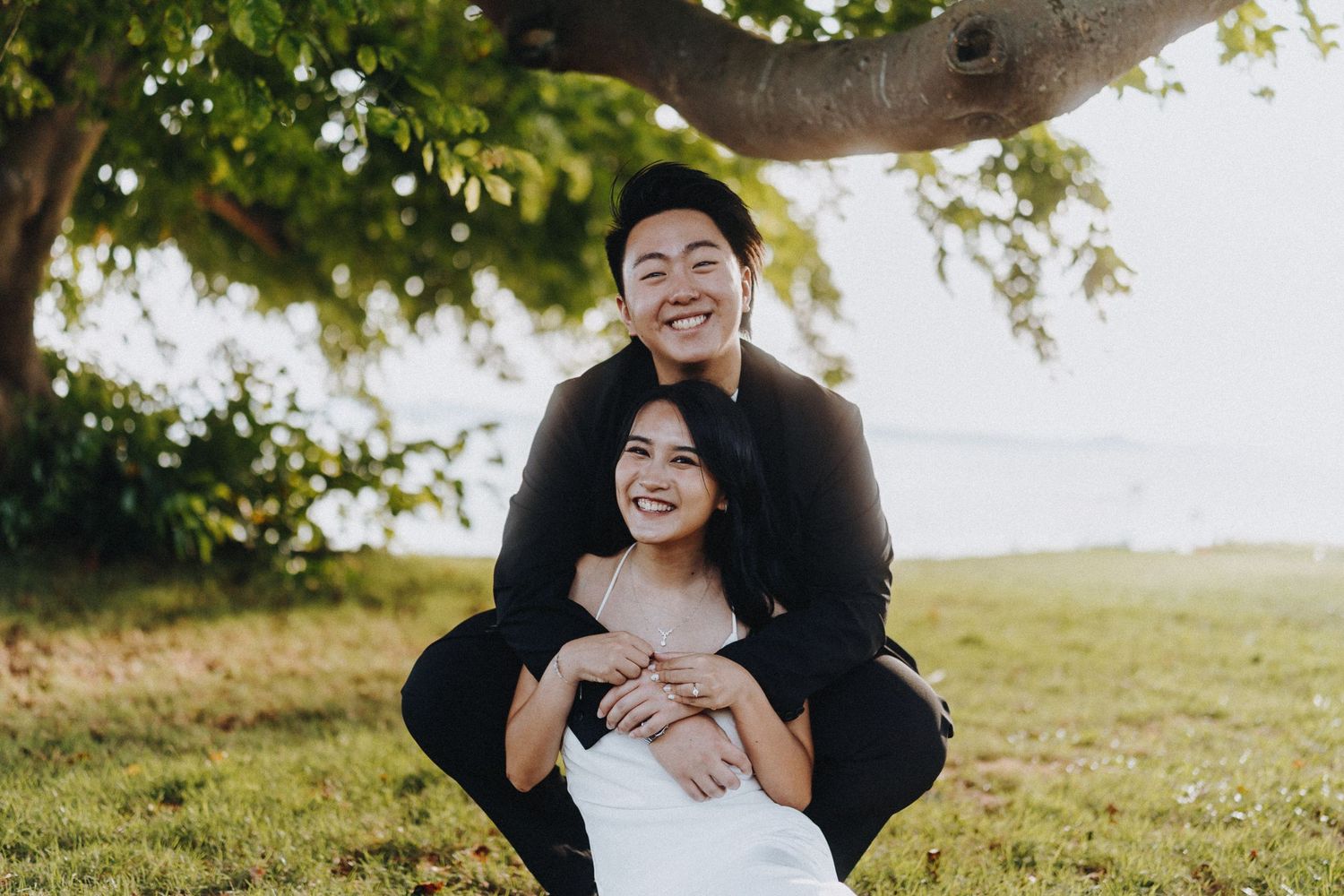 Couple sharing playful moments under a tree with sunlight filtering through leaves.
