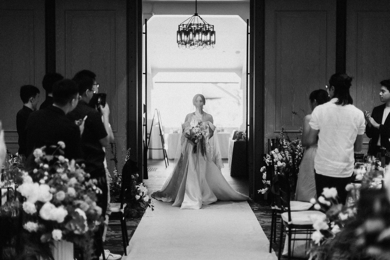 A wedding ceremony setup with a long aisle flanked by floral arrangements and chairs in a grand indoor venue.