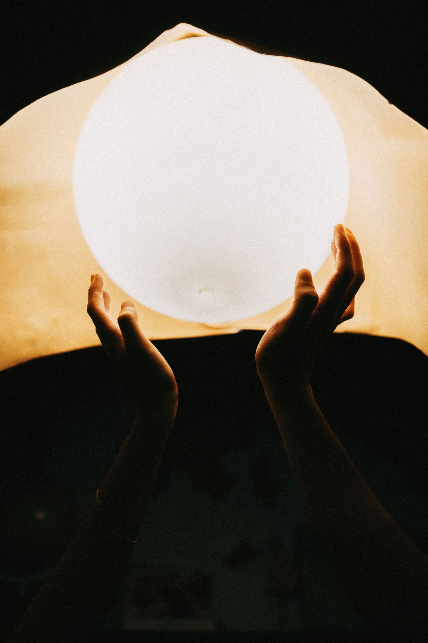 A sequence of silhouetted hands lighting a white paper lantern against a dark background.