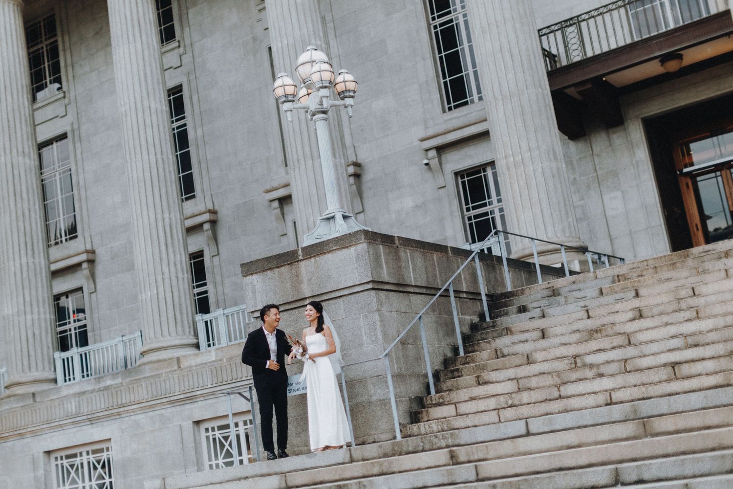 Wedding couple standing on grand stone steps of classical building.