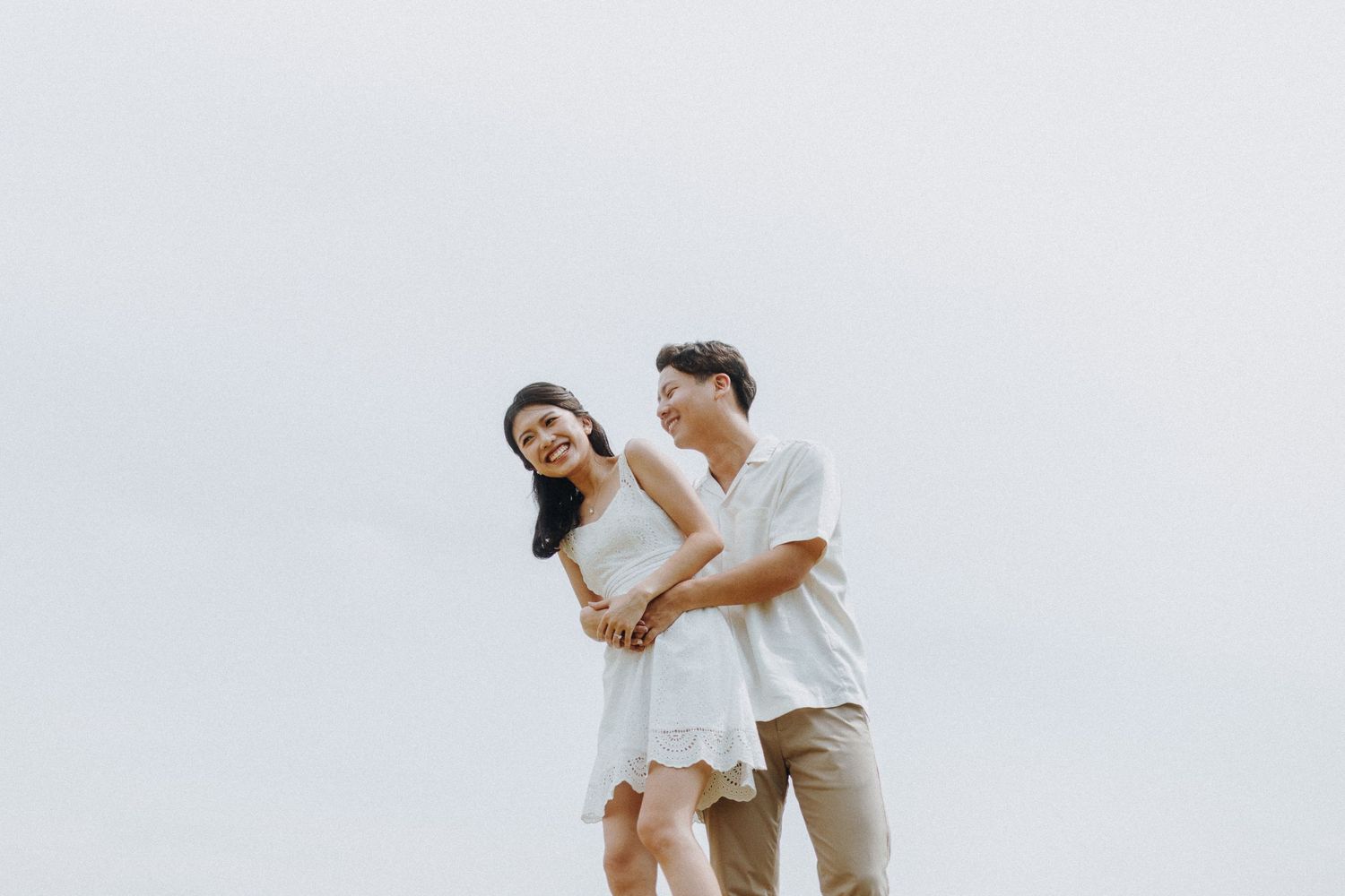 Romantic casual photoshoot outdoors with a couple in white and beige outfits.