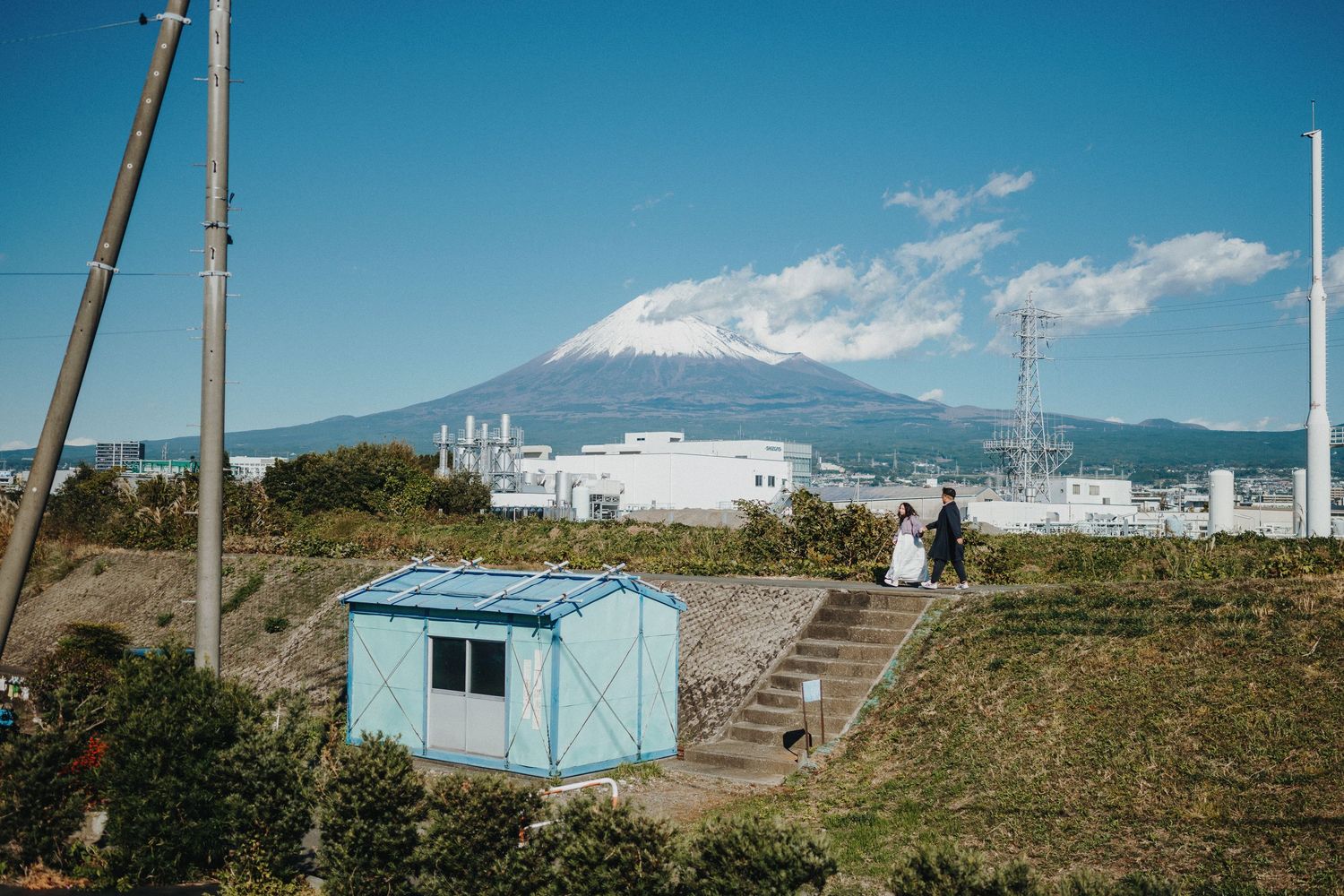 Panoramic view of Mount Fuji with industrial buildings and a staircase in the foreground.