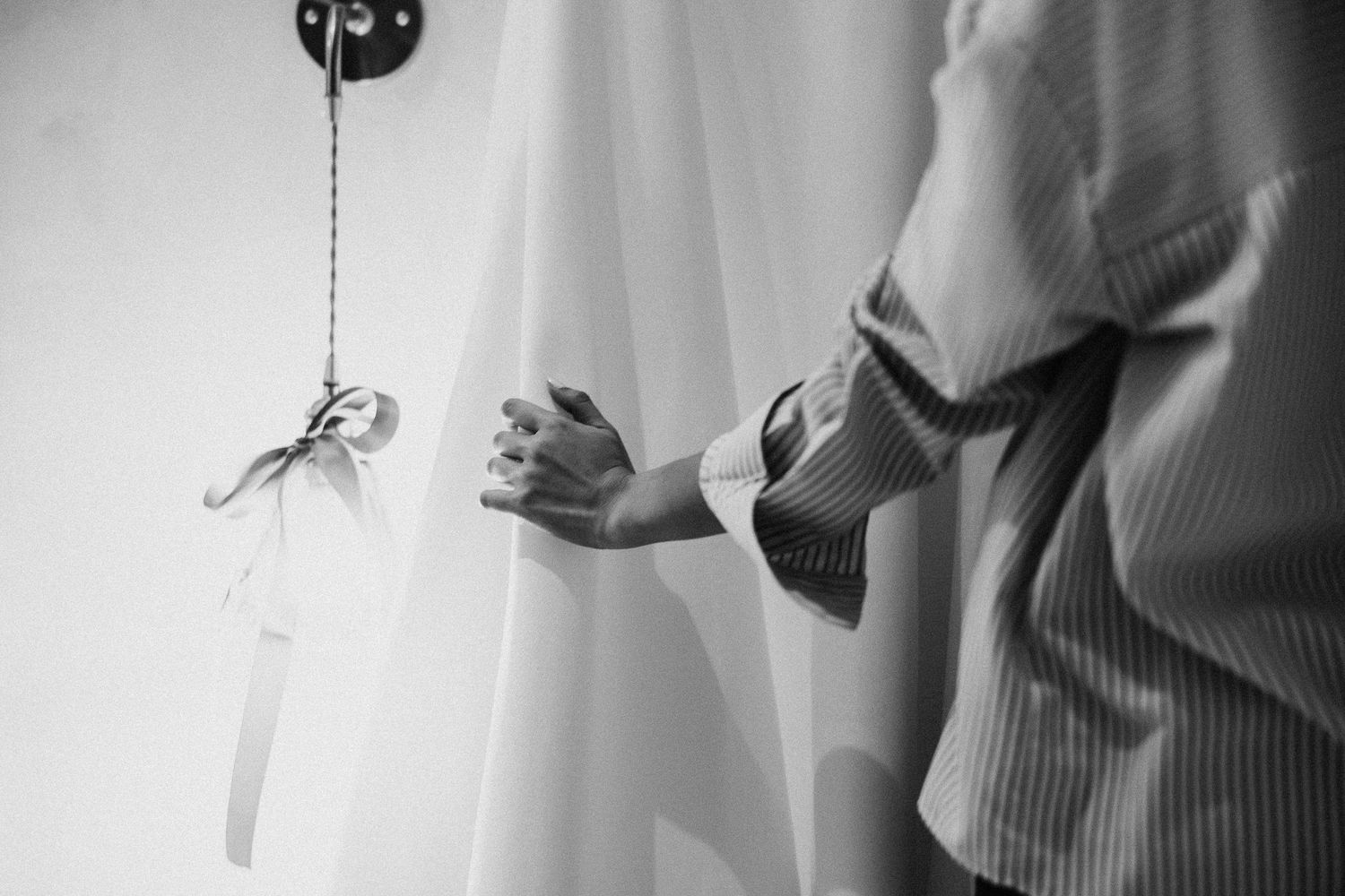 Black and white image shows a dangling key hanging from a string being grasped at by someone's hand.