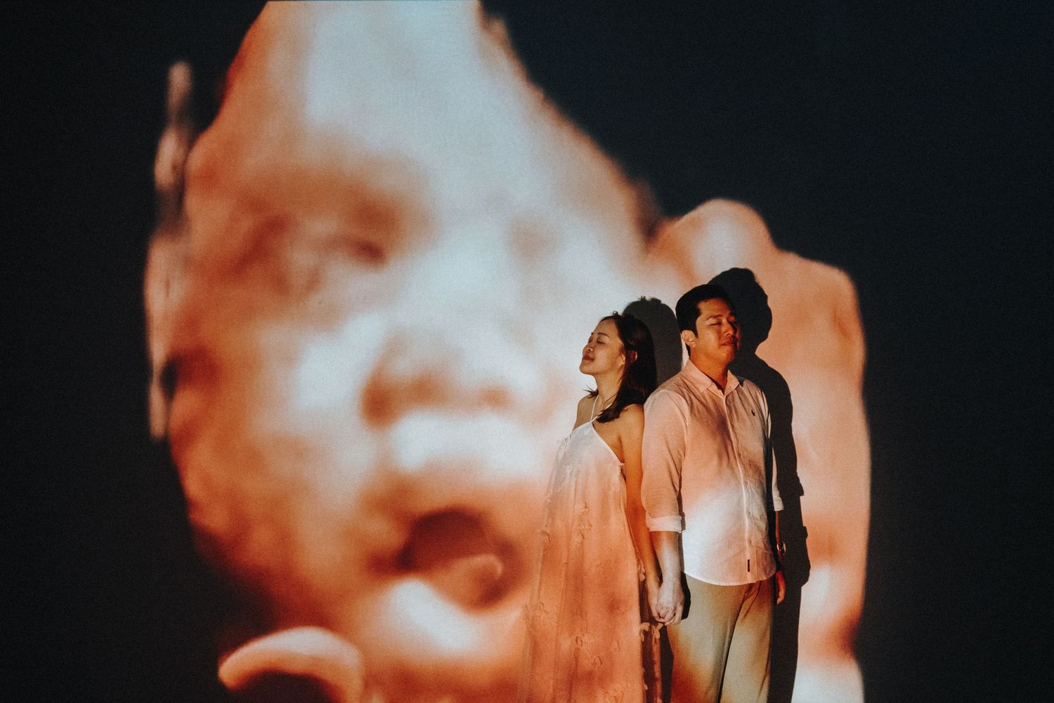 Couple standing against dramatic orange backlit projection creating artistic silhouettes.