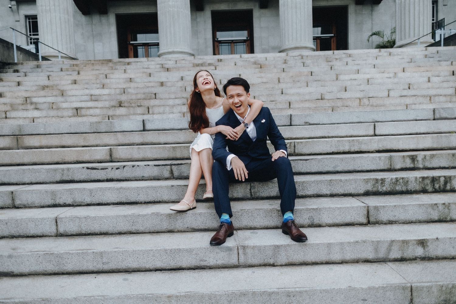 Couple shares romantic moments on white stone steps of a grand building.