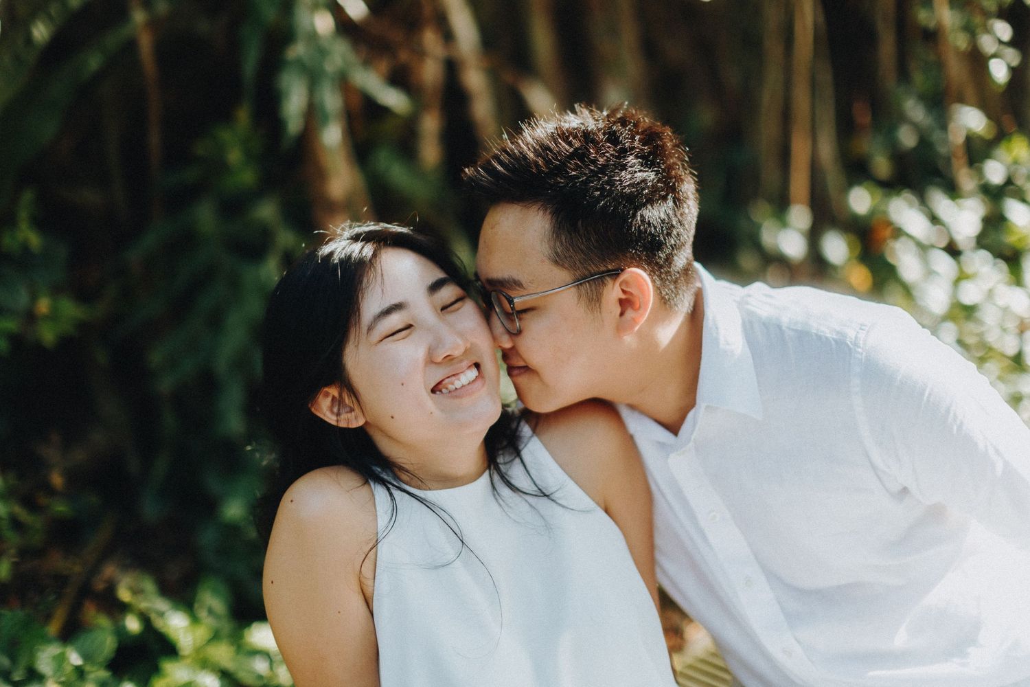 A couple shares intimate moments in a romantic outdoor photo shoot with natural lighting and greenery surroundings.