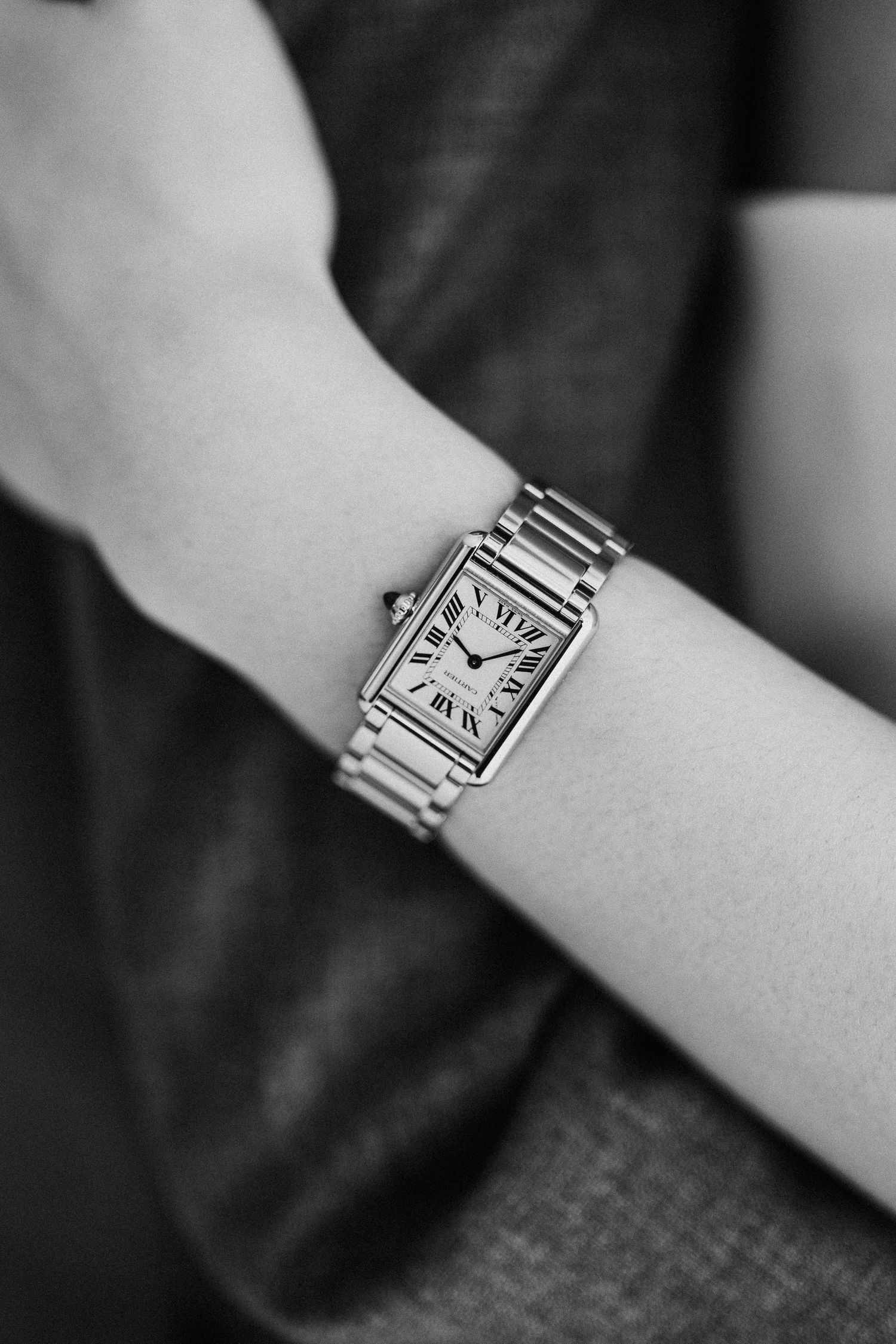 A classic silver Cartier Tank watch with a white square dial and metal bracelet shown on a wrist in black and white.