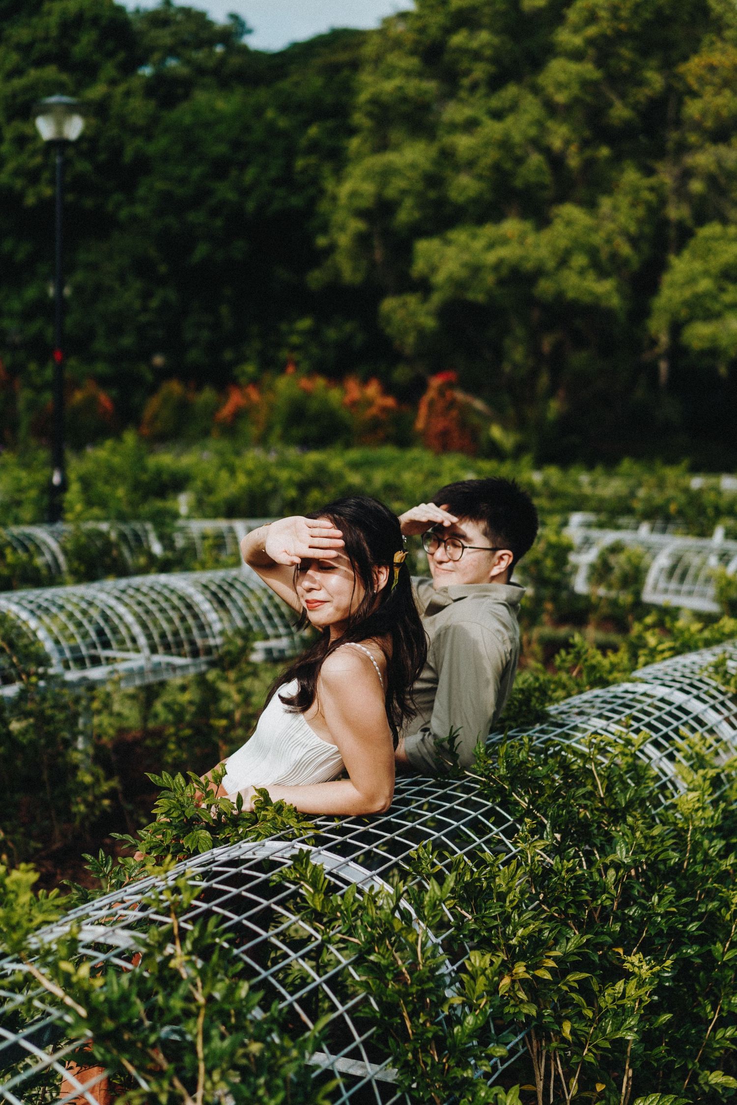A couple poses back-to-back in a garden with decorative wire frames and lush greenery.