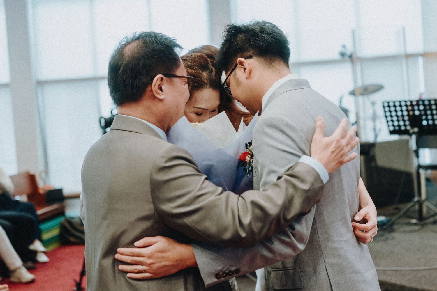Three people share an emotional embrace during a wedding ceremony.
