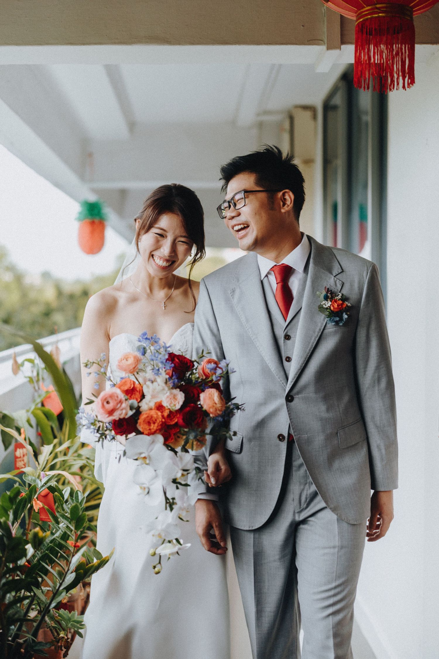 A newlywed couple in wedding attire share a joyful moment with a colorful bouquet on a balcony.
