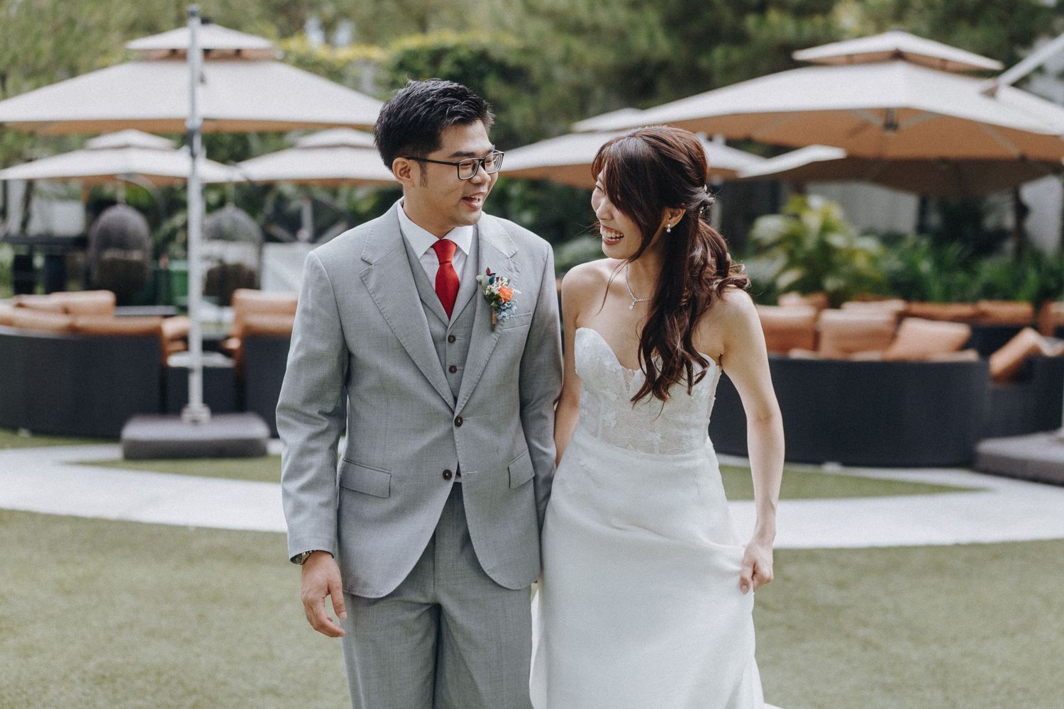 A couple shares a romantic moment on a sunny lawn with patio umbrellas in the background.