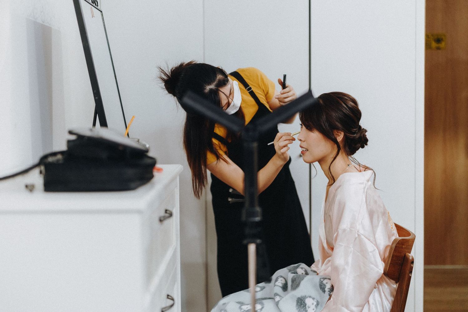A bridal party helps the bride get ready in a warm-lit room before the wedding ceremony.