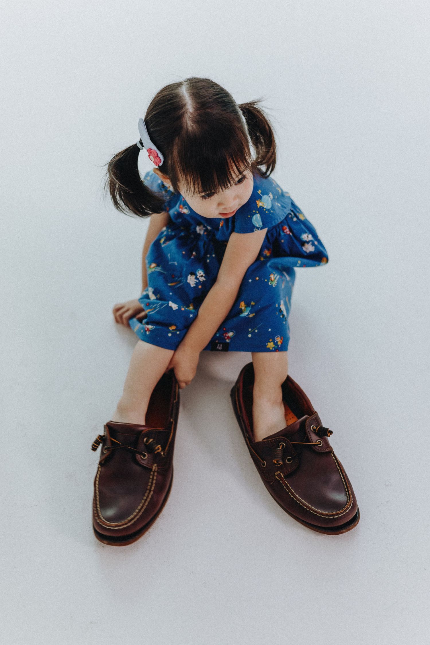 Close-up of small brown leather boat shoes worn with a blue patterned dress.