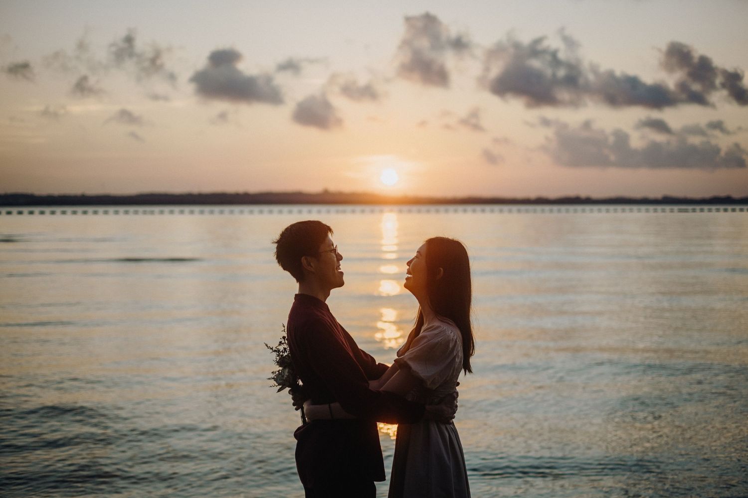 Couple silhouetted against a golden sunset over the ocean while sharing an intimate moment on the beach.
