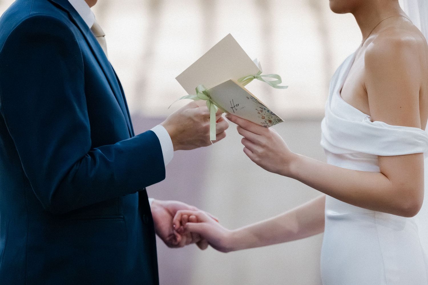 Bride and groom exchanging vows cards while holding hands during outdoor wedding ceremony.