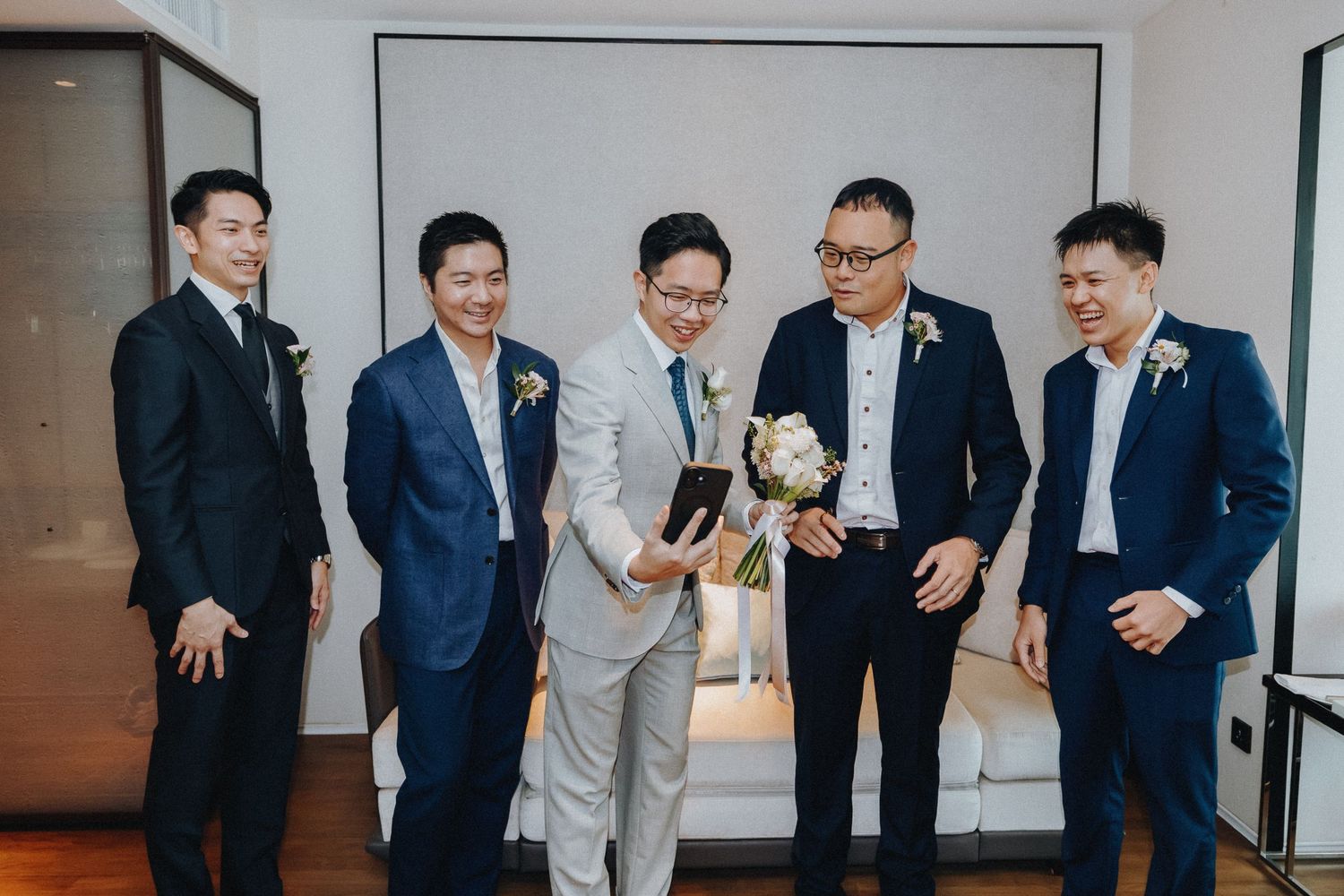 Groomsmen in suits sharing laughter and candid moments during wedding preparations.