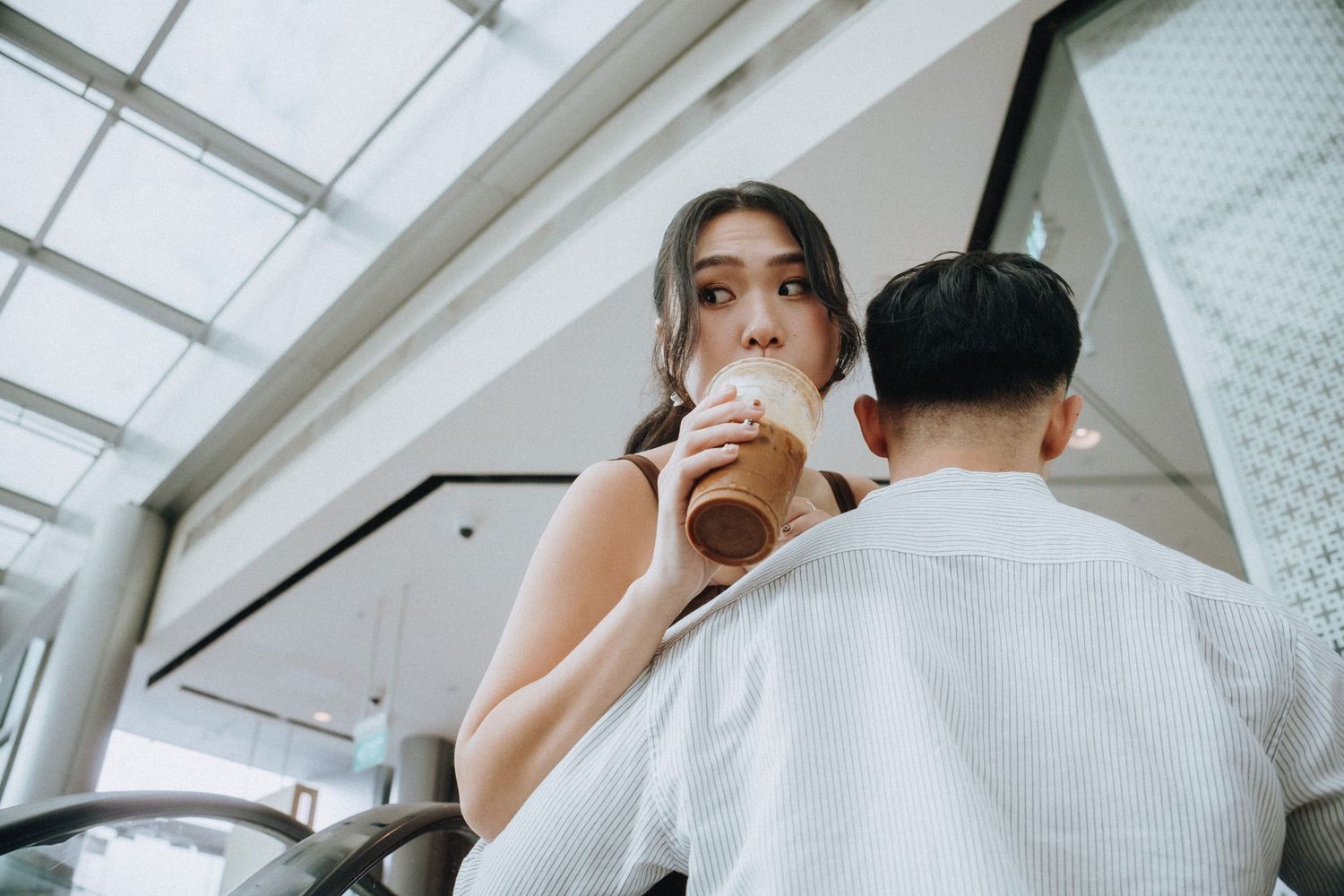 Young couple on a date at a cafe, woman sipping an iced drink while man sits across from her indoors.