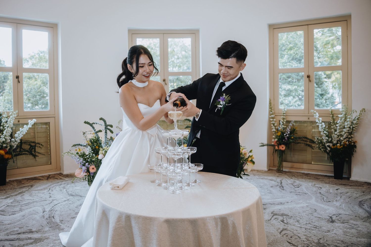 Bride and groom pouring champagne tower together at elegant wedding reception venue.