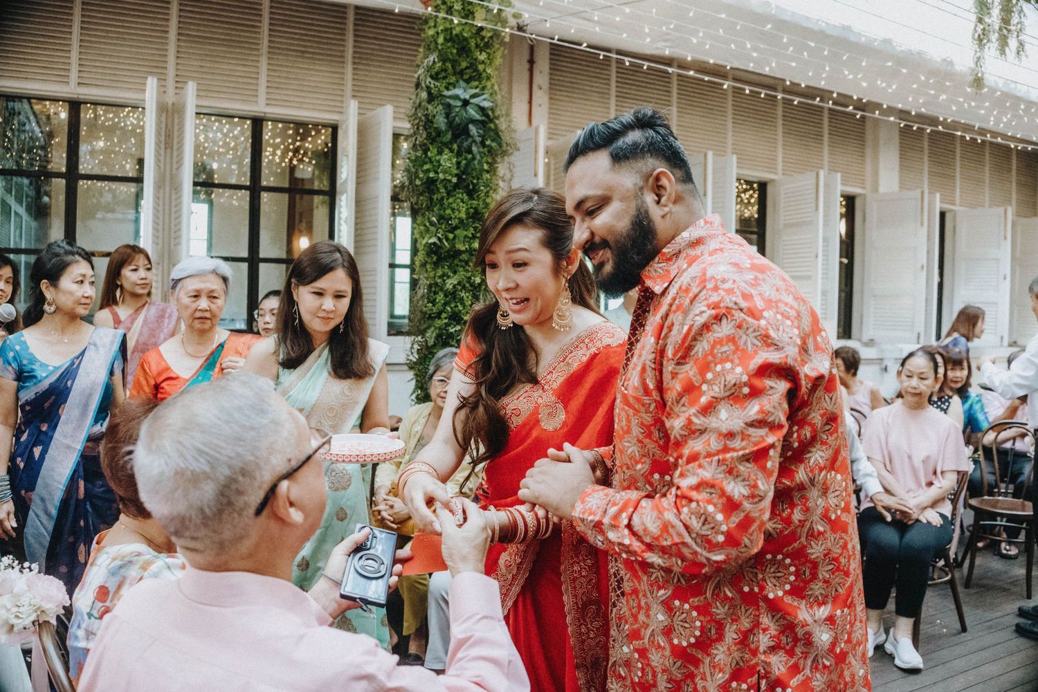 Couple in matching red outfits during traditional Chinese tea ceremony with guests.