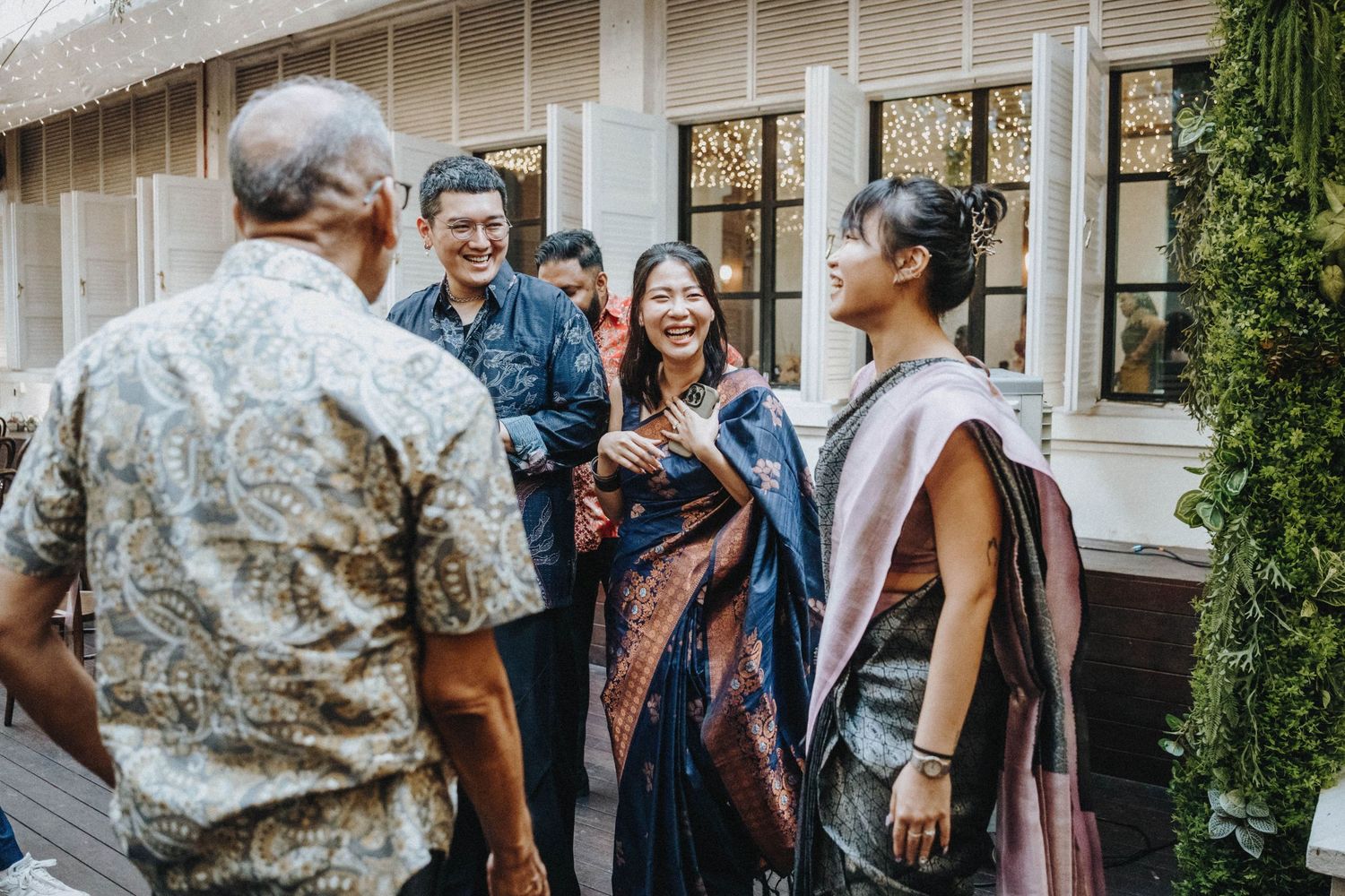 Guests in traditional Indian and batik attire socializing at outdoor wedding venue.
