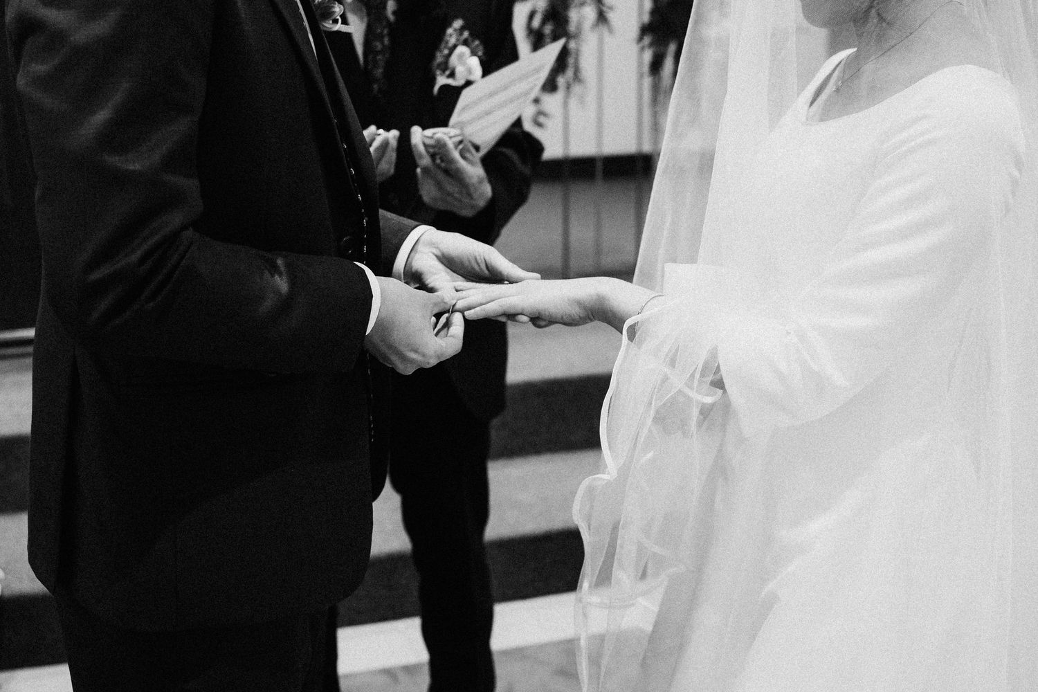 Groom placing wedding ring on brides finger during black and white church ceremony.
