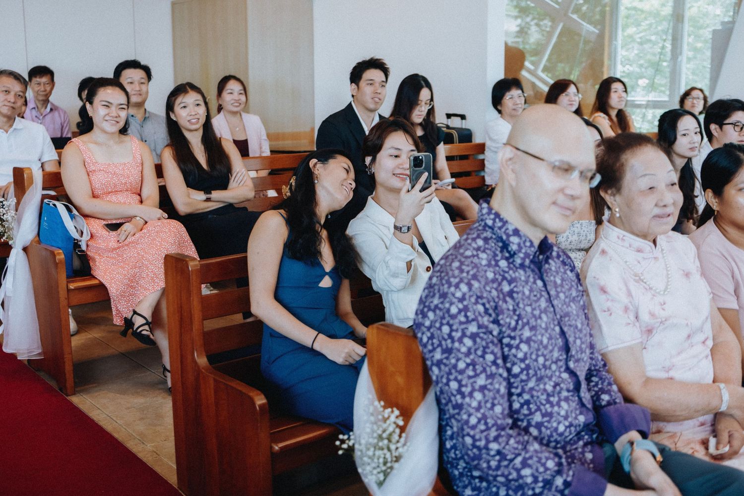 Wedding guests seated in church pews smile and react emotionally during a wedding ceremony.