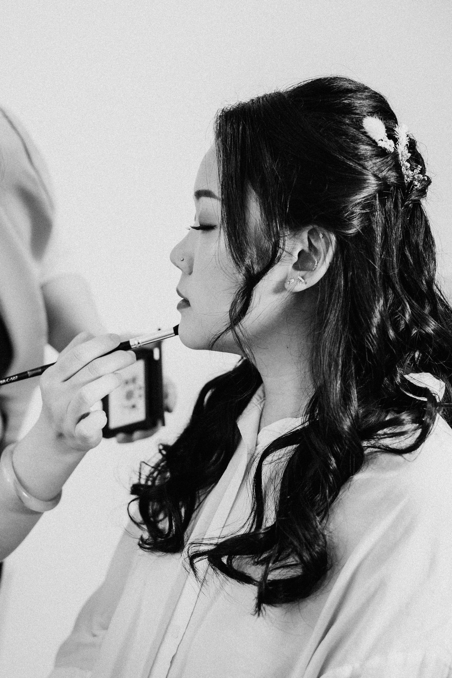 Black and white photo of a bride having lipstick applied by a makeup artist on her wedding day.
