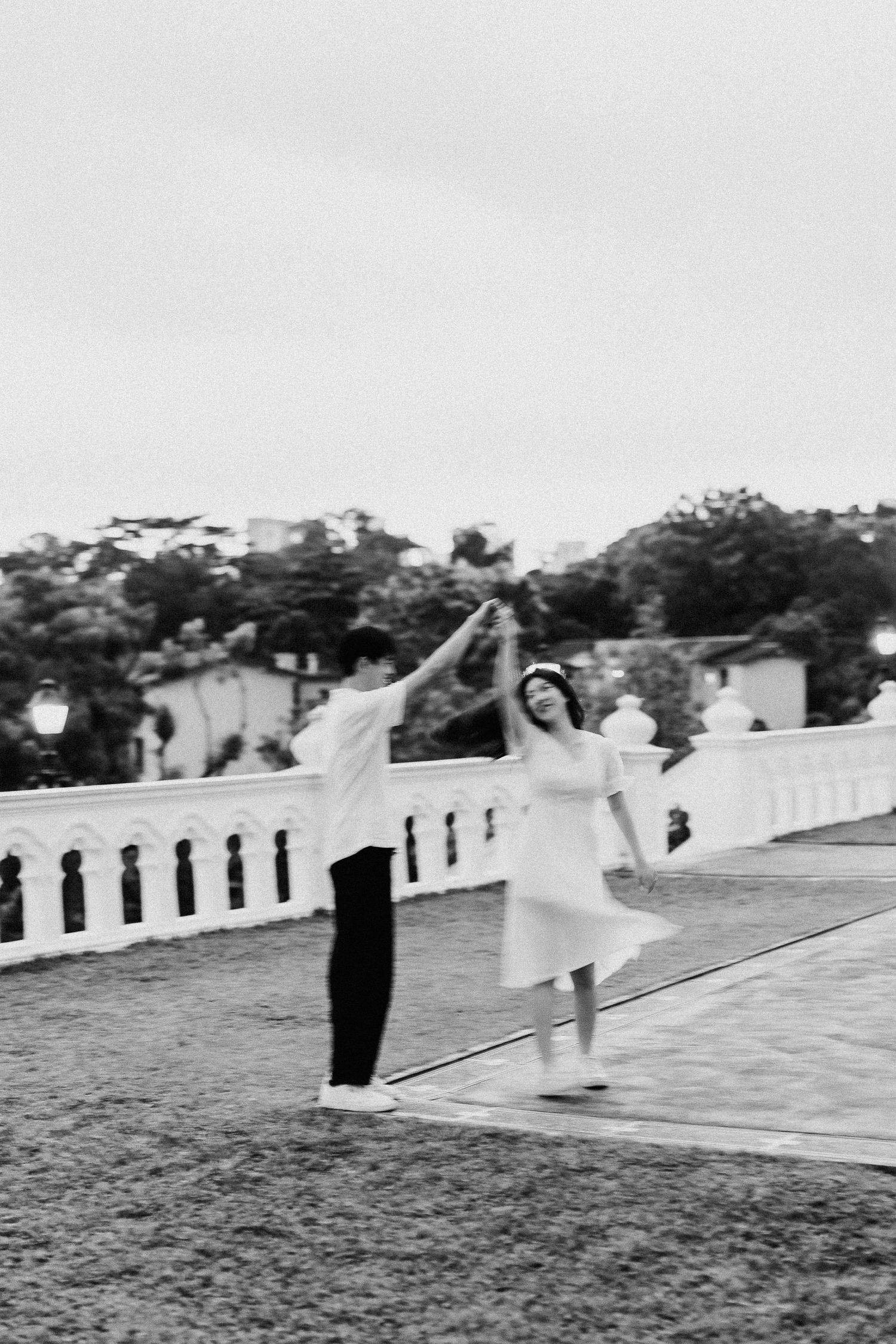 A black and white photo of a couple dancing playfully on a terrace with white balustrades.
