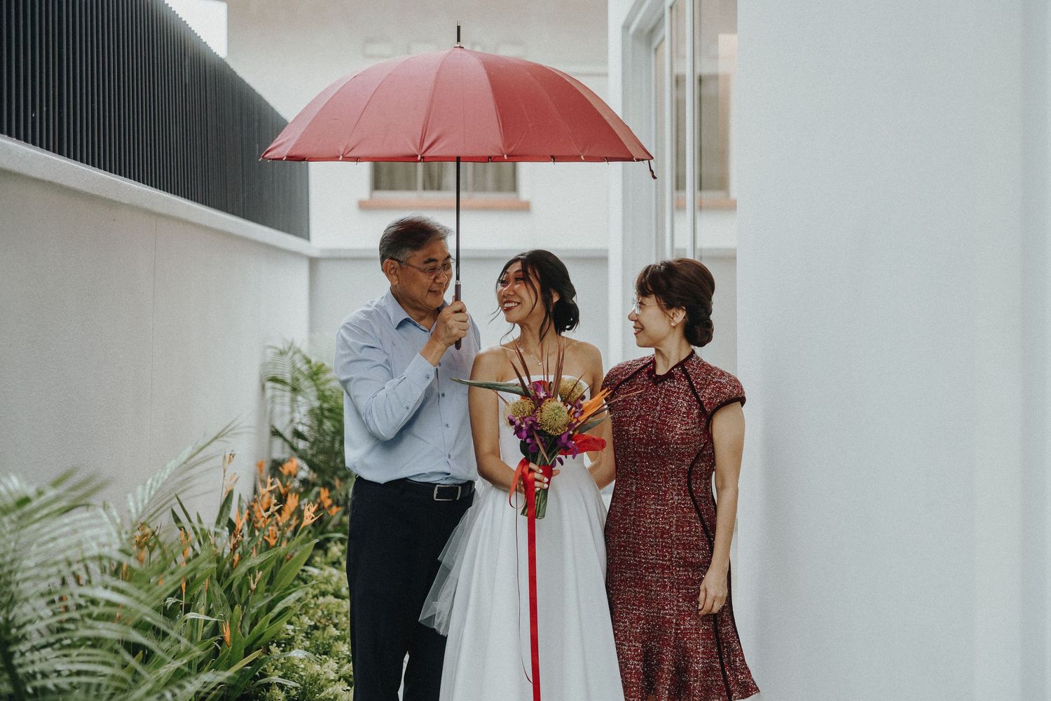 A wedding couple stands close under a pink umbrella during their intimate photo session.