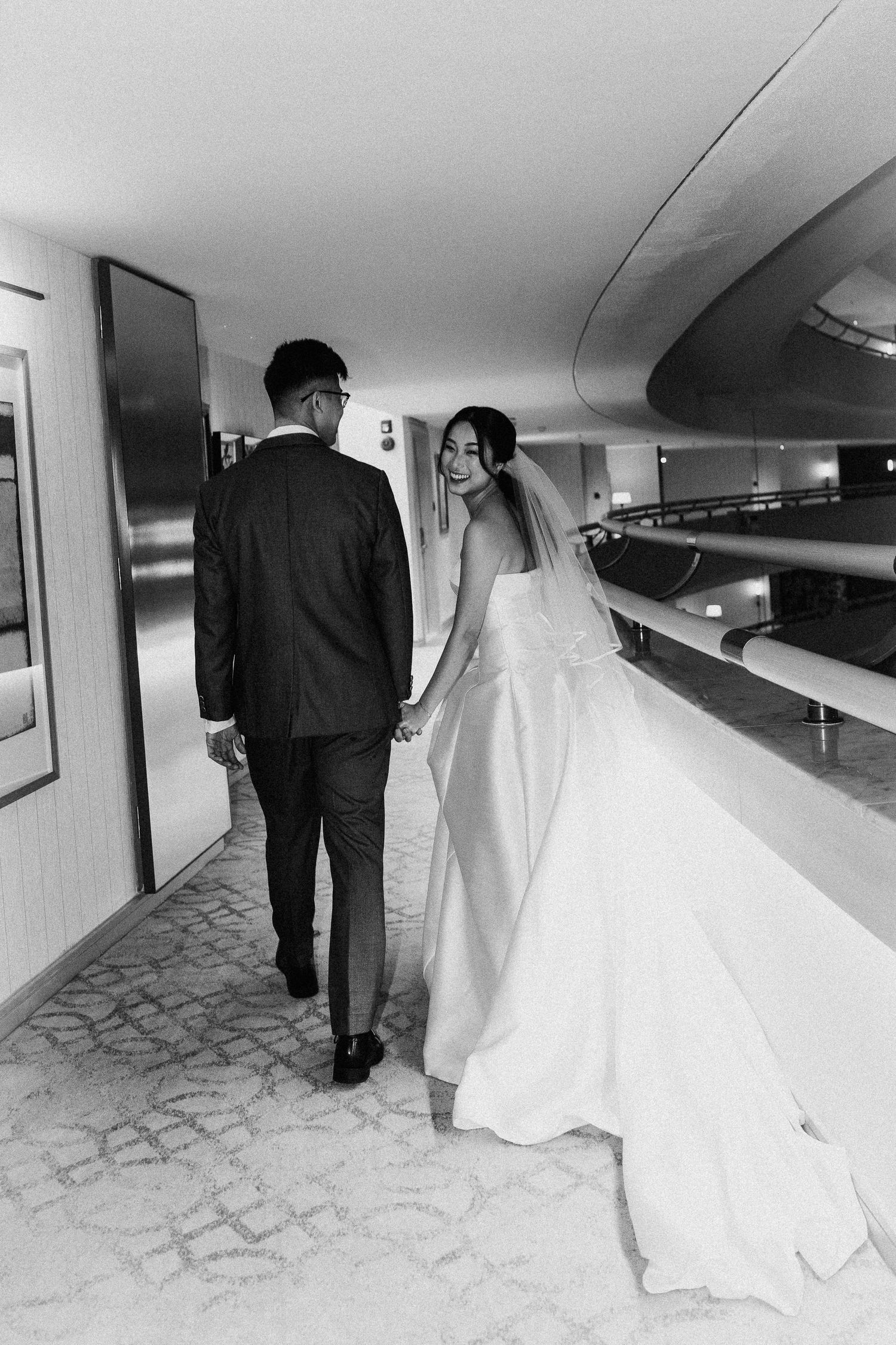 A couple walking down a hallway in wedding attire captured in black and white.