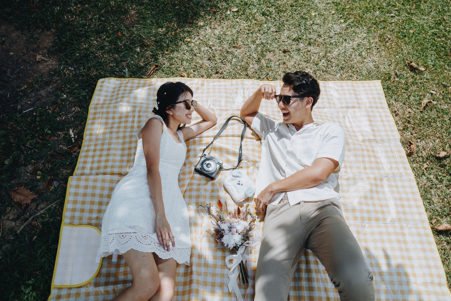 A couple having a picnic on a checkered blanket with their dog outdoors.