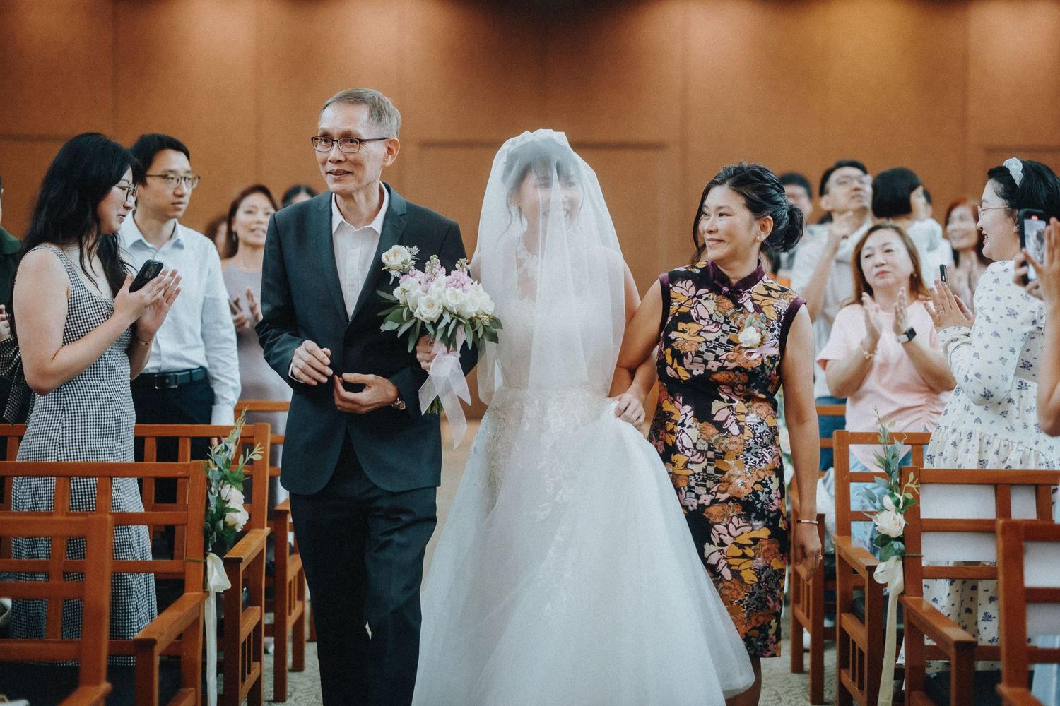 Wedding ceremony in progress with guests standing in wooden chairs while applauding.