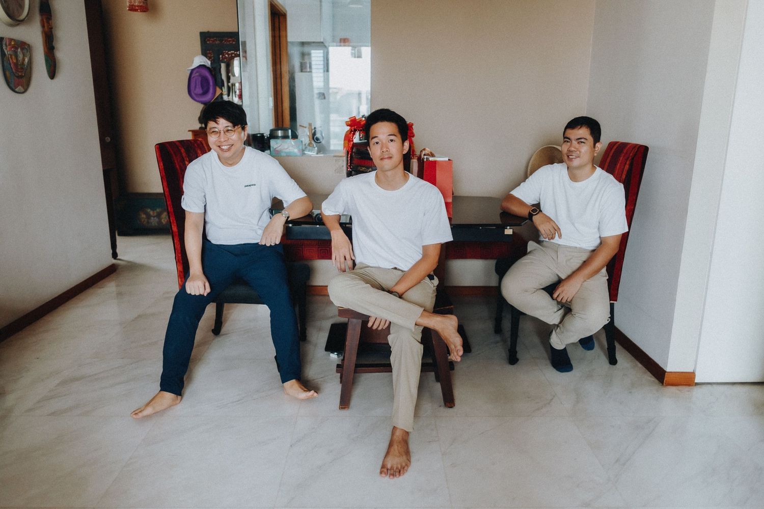 Three people in white shirts relaxing casually on chairs in a minimalist interior room setting.
