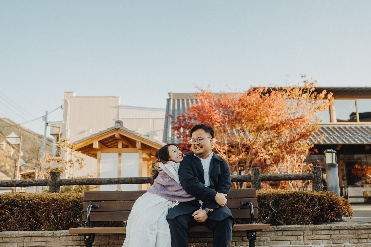 Couple walking through a traditional Japanese street with autumn colors in the background.