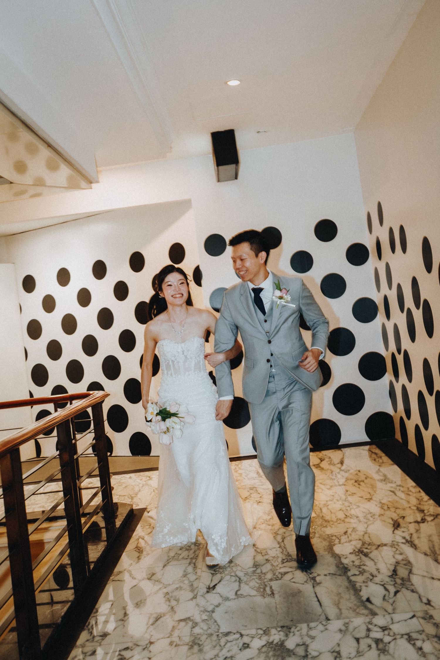 A couple walks down a stairwell with black polka dot walls during their wedding celebration.