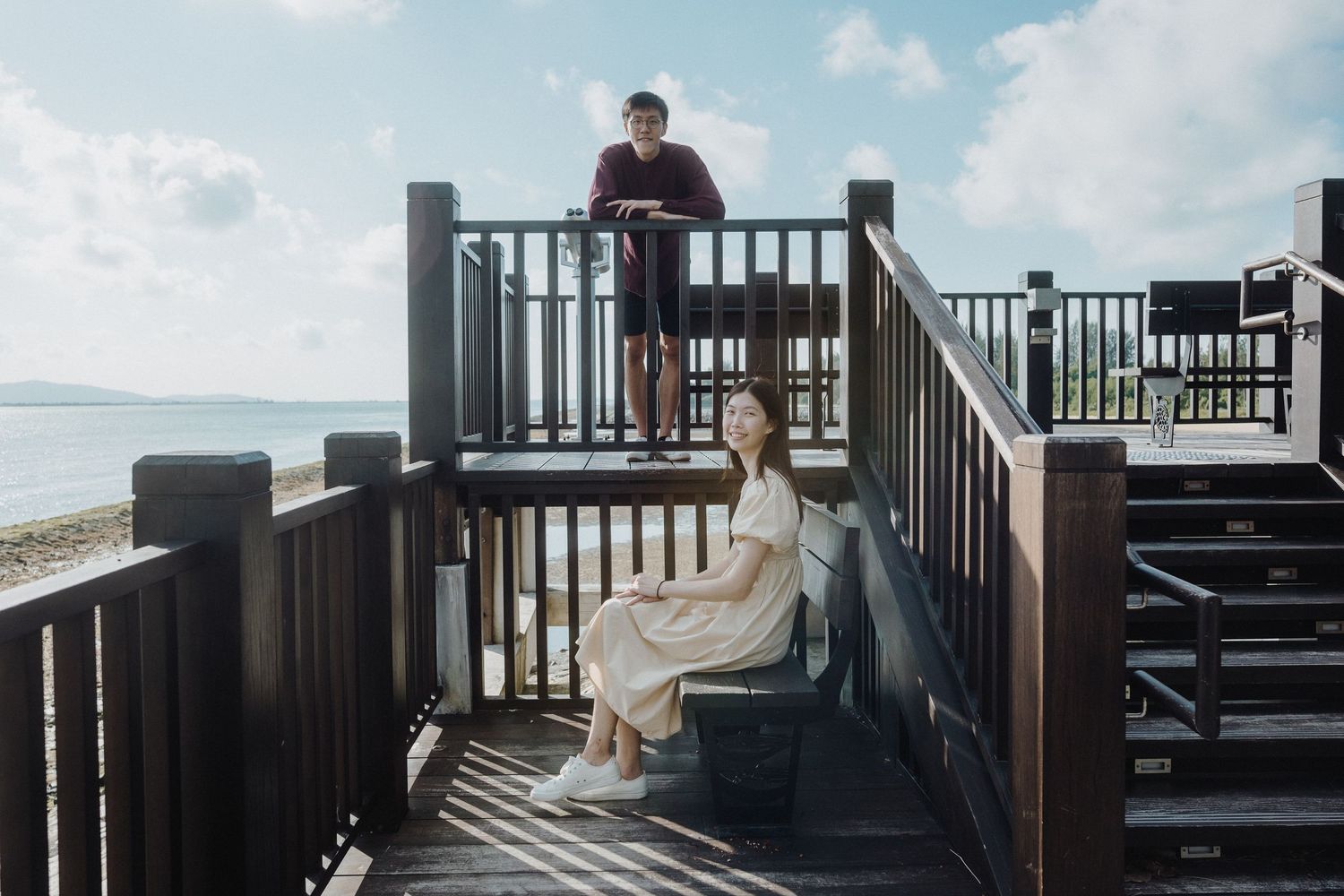 A couple sits together on wooden deck stairs overlooking a scenic view.