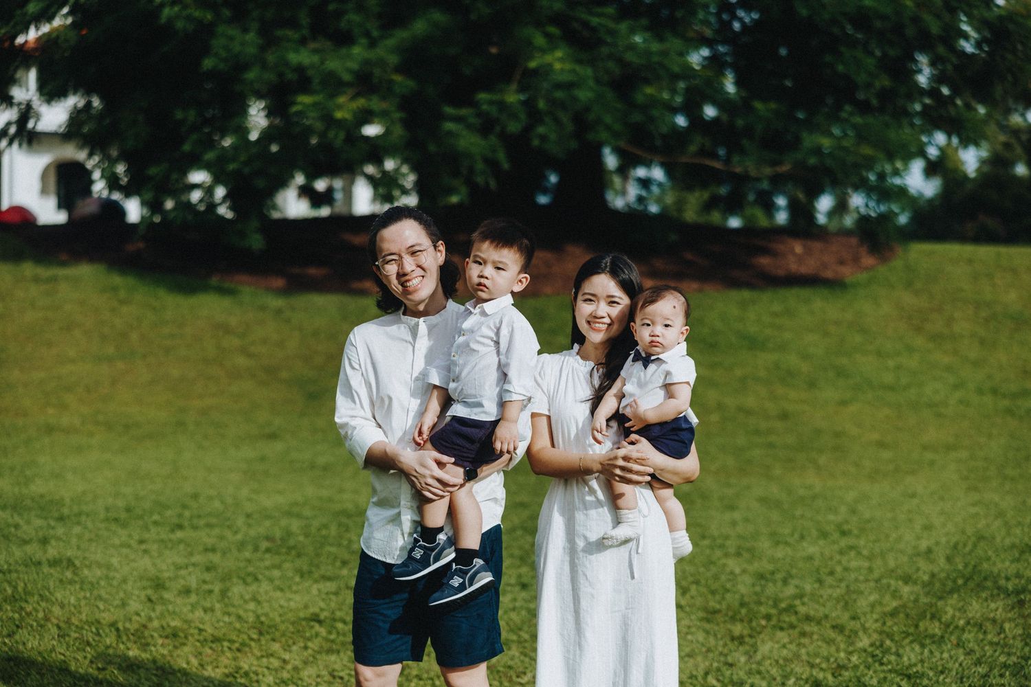 A family stands together on a lush green lawn on a summer day wearing white and navy casual clothing.