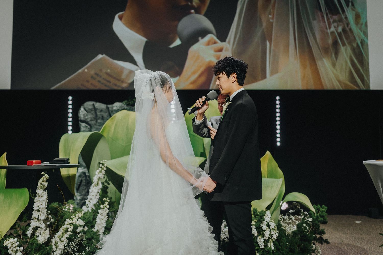 A wedding ceremony scene with white floral decorations and green accent lighting.