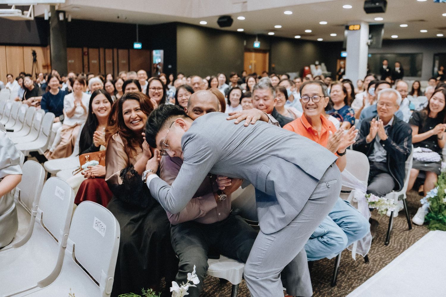 Wedding guests celebrate and cheer during an emotional moment at a ceremony with white chairs.