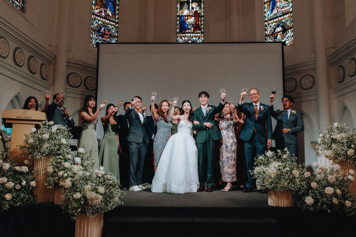 Wedding party celebrating at church altar with raised glasses and floral arrangements.