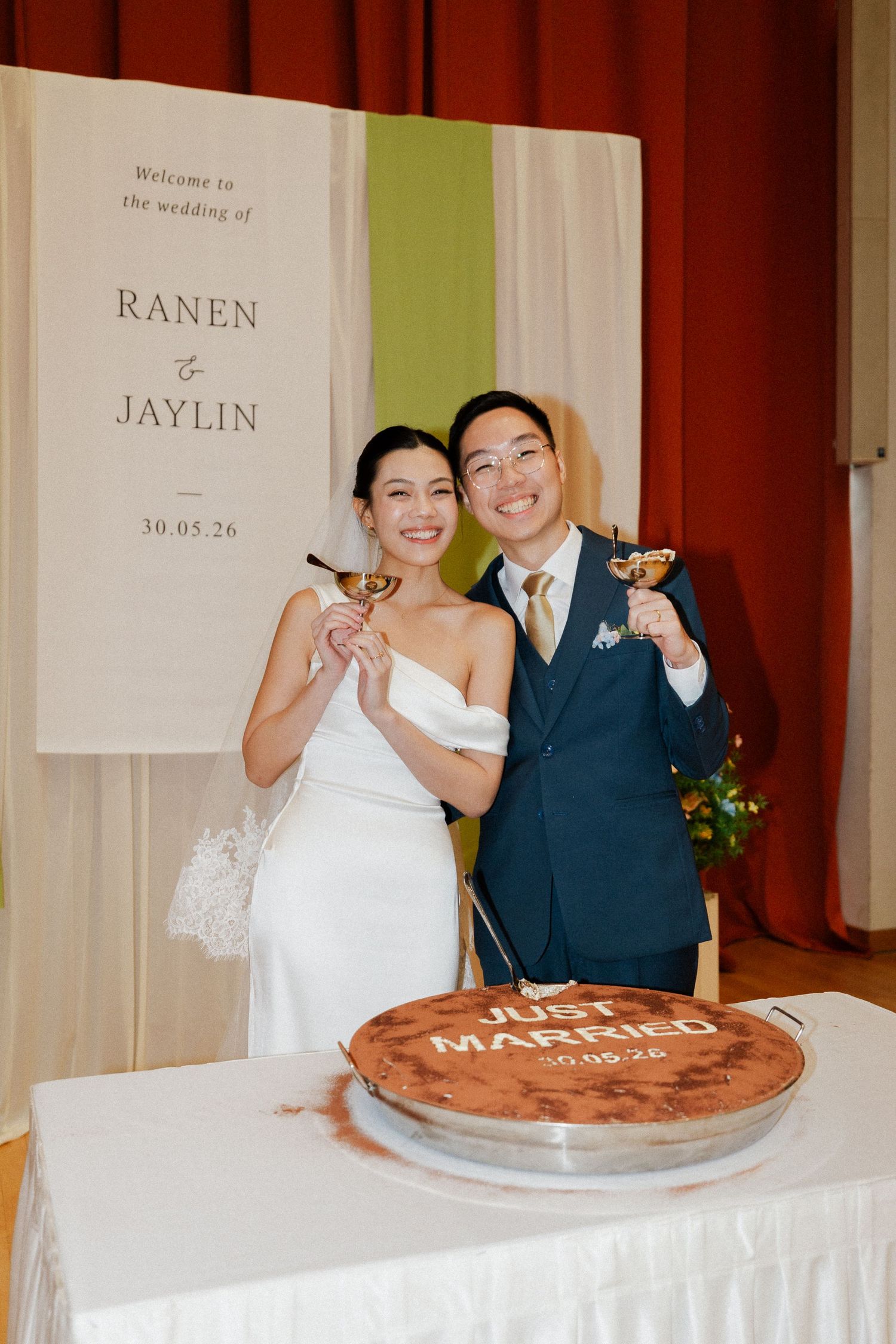 Newlyweds Ranen and Jaylin toast with cocktails beside a Just Married cake at their wedding reception.