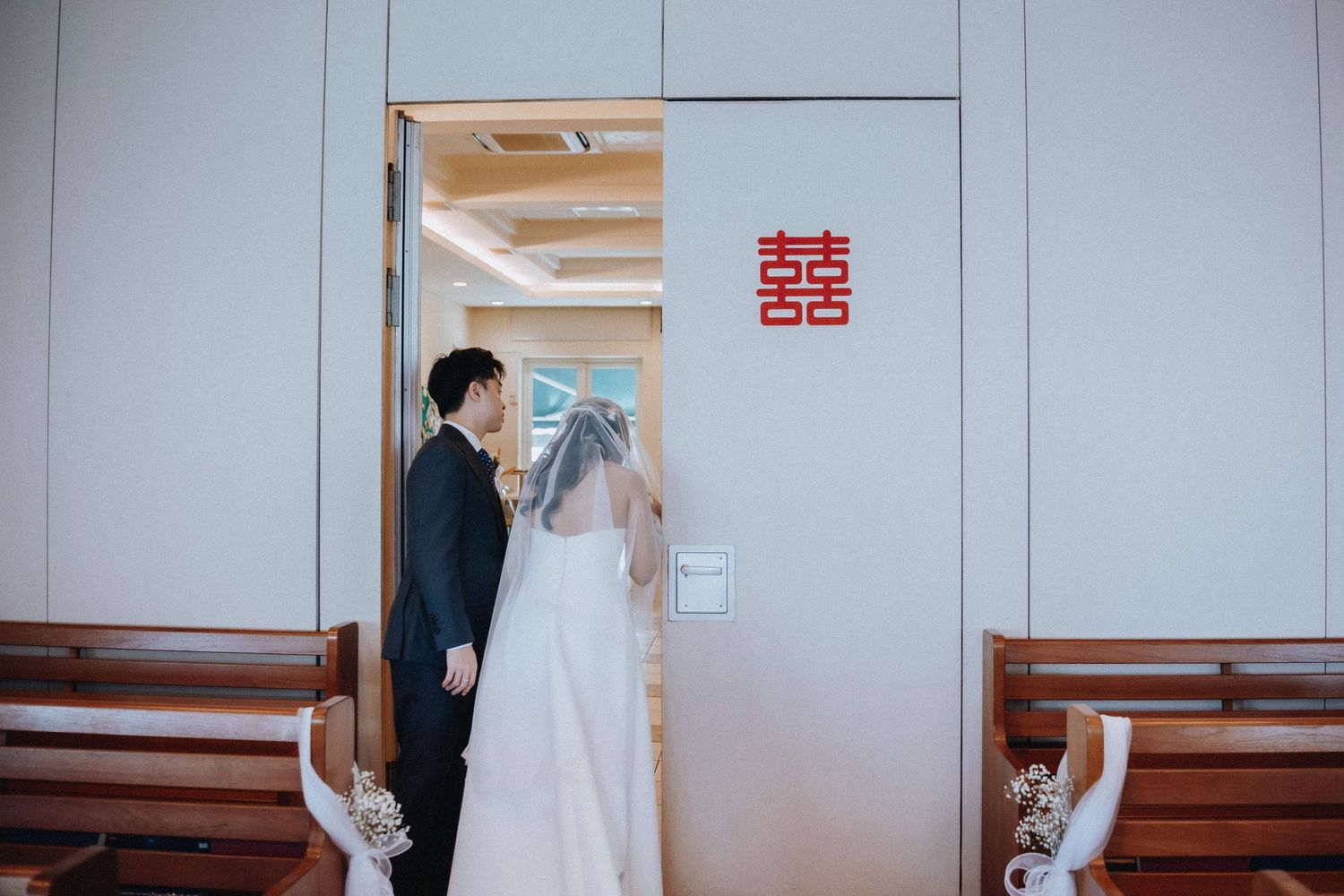 Bride and groom standing at doorway with red double happiness symbol at their Chinese wedding ceremony.