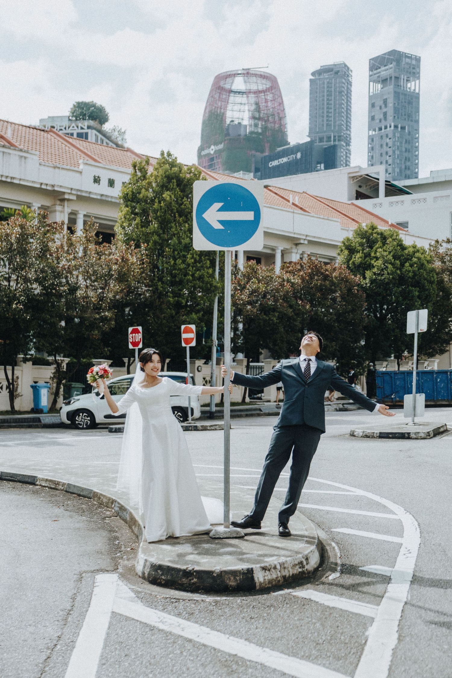Joyful bride and groom posing playfully at urban street intersection with city skyline backdrop.